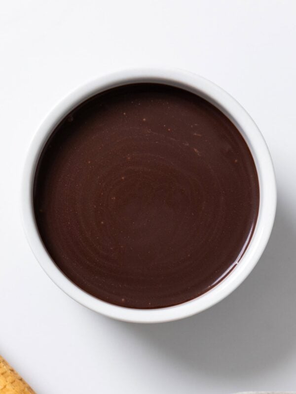 White bowl filled with chocolate hot fudge sauce on white surface.