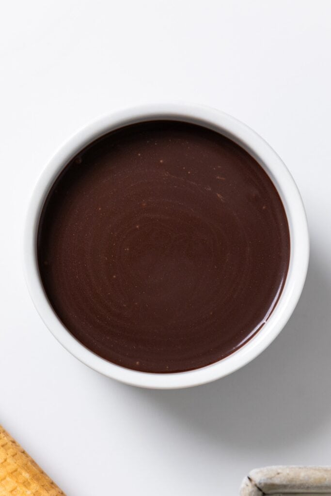White bowl filled with chocolate hot fudge sauce on white surface.