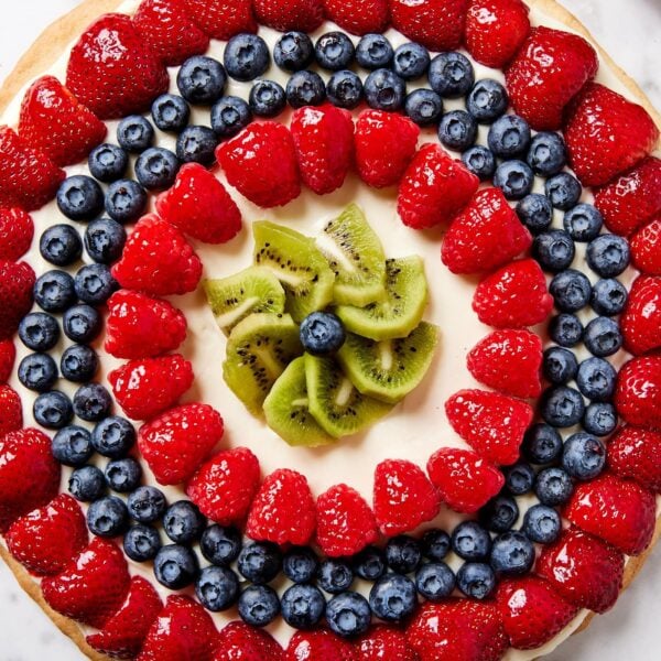 Fruit pizza sitting on white marble surface with rings of strawberries, raspberries, and blueberries on top.