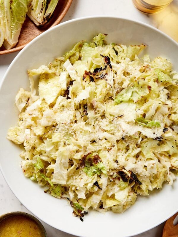 Large white bowl filled with cabbage salad with charred bits topped with Parmesan cheese all on white surface.