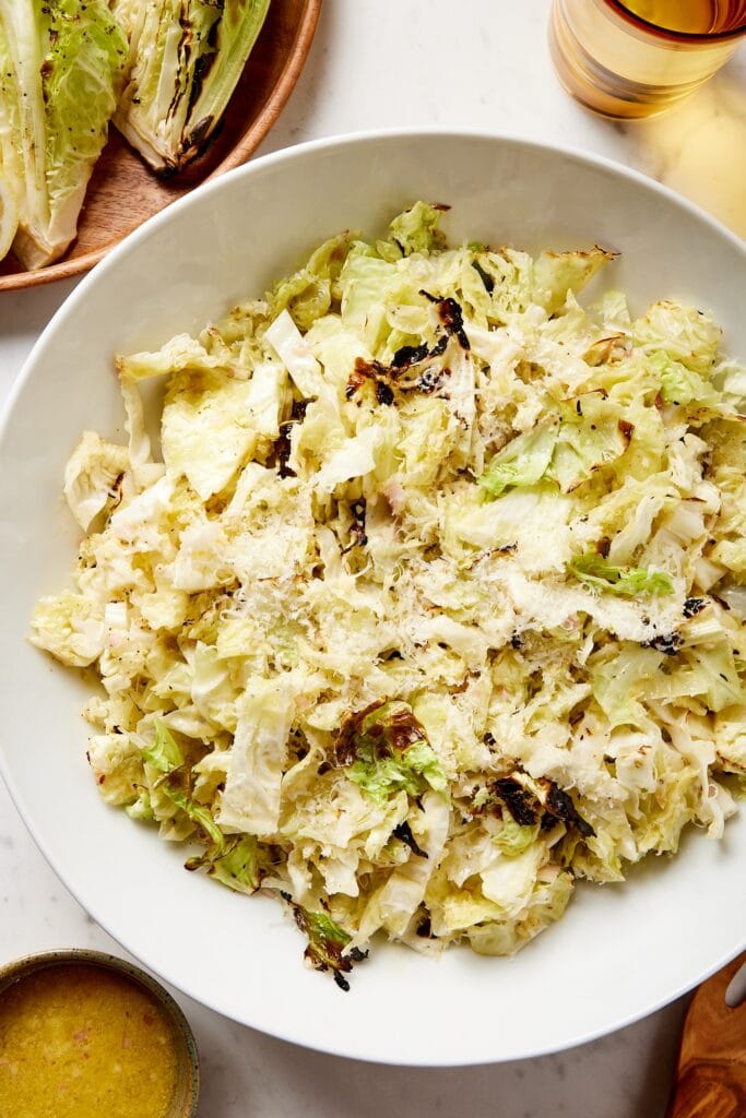 Large white bowl filled with cabbage salad with charred bits topped with Parmesan cheese all on white surface.