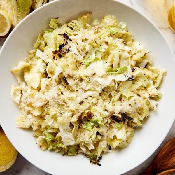 Large white bowl filled with chopped cabbage topped with Parmesan cheese on white marble surface.