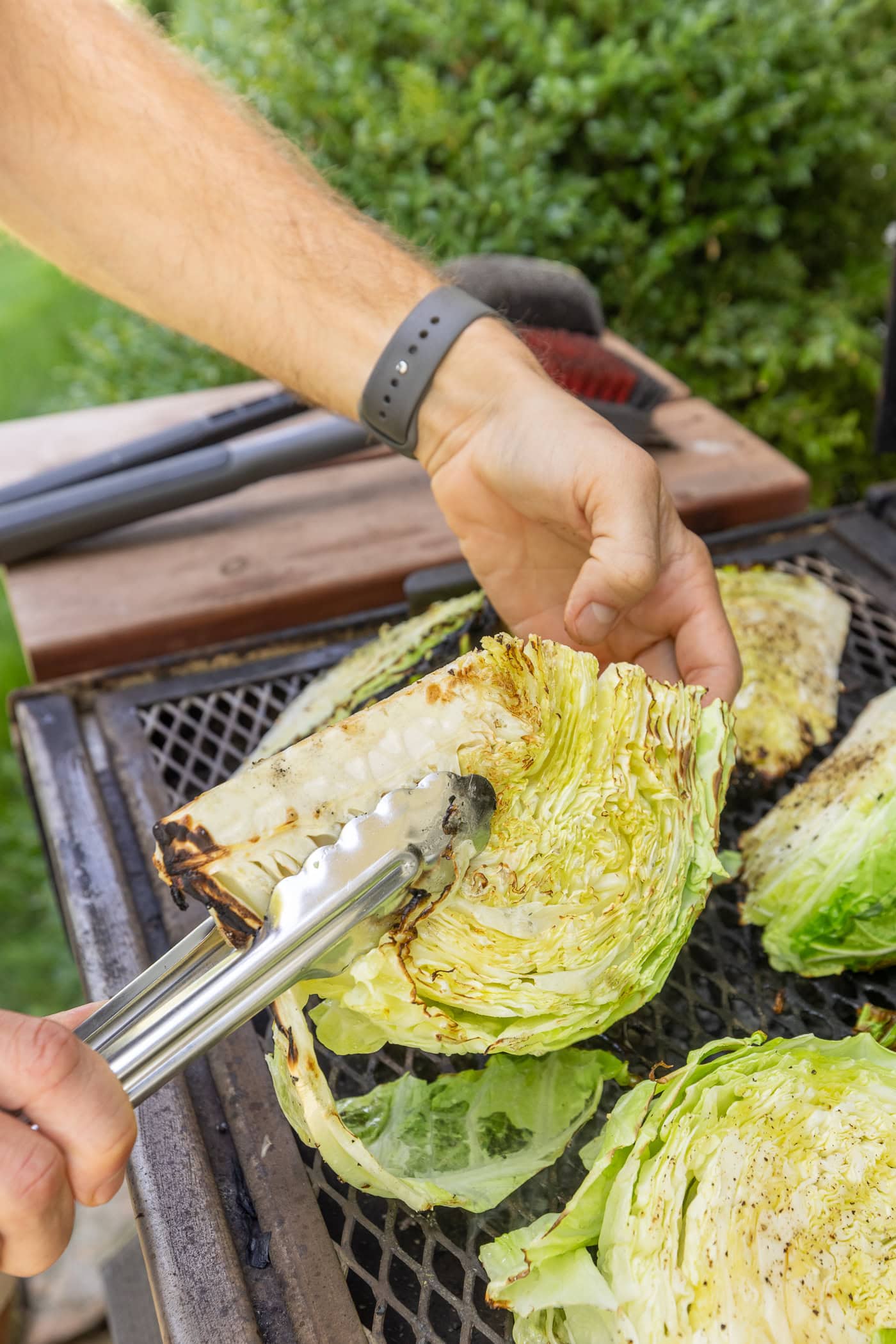 Hand using tongs to flip over grilled cabbage with char on a grill.