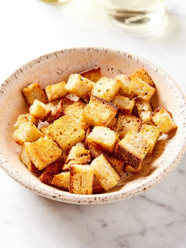 White stoneware bowl filled with homemade croutons with crispy browned exterior.