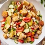 Large white bowl filled with panzanella with tomatoes, bread cubes, cucumbers, mozzarella cheese, and more.
