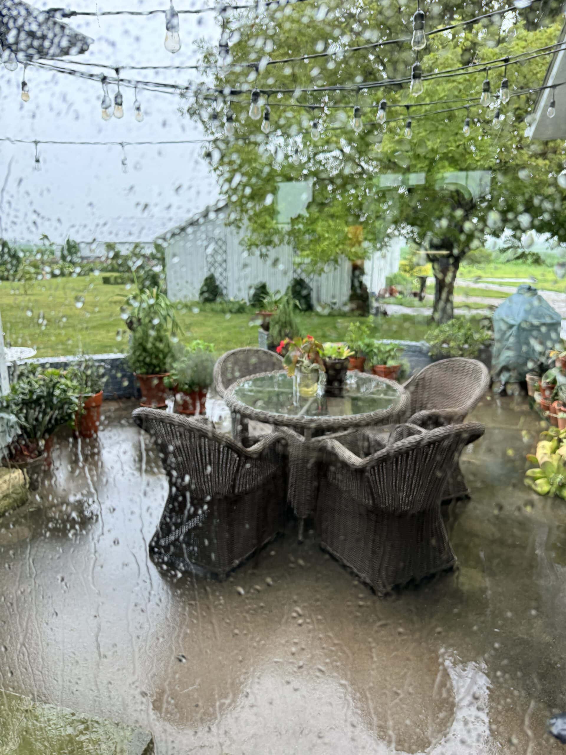 Rain dripping down a window looking out onto a patio with outdoor furniture.