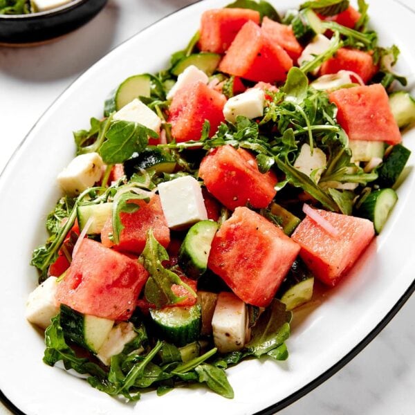 White plate filled with cubes of watermelon and feta and arugula mixed together for a summer salad.
