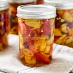 Jar of canned pickled peppers sitting on a towel with more pickle jars to the sides.