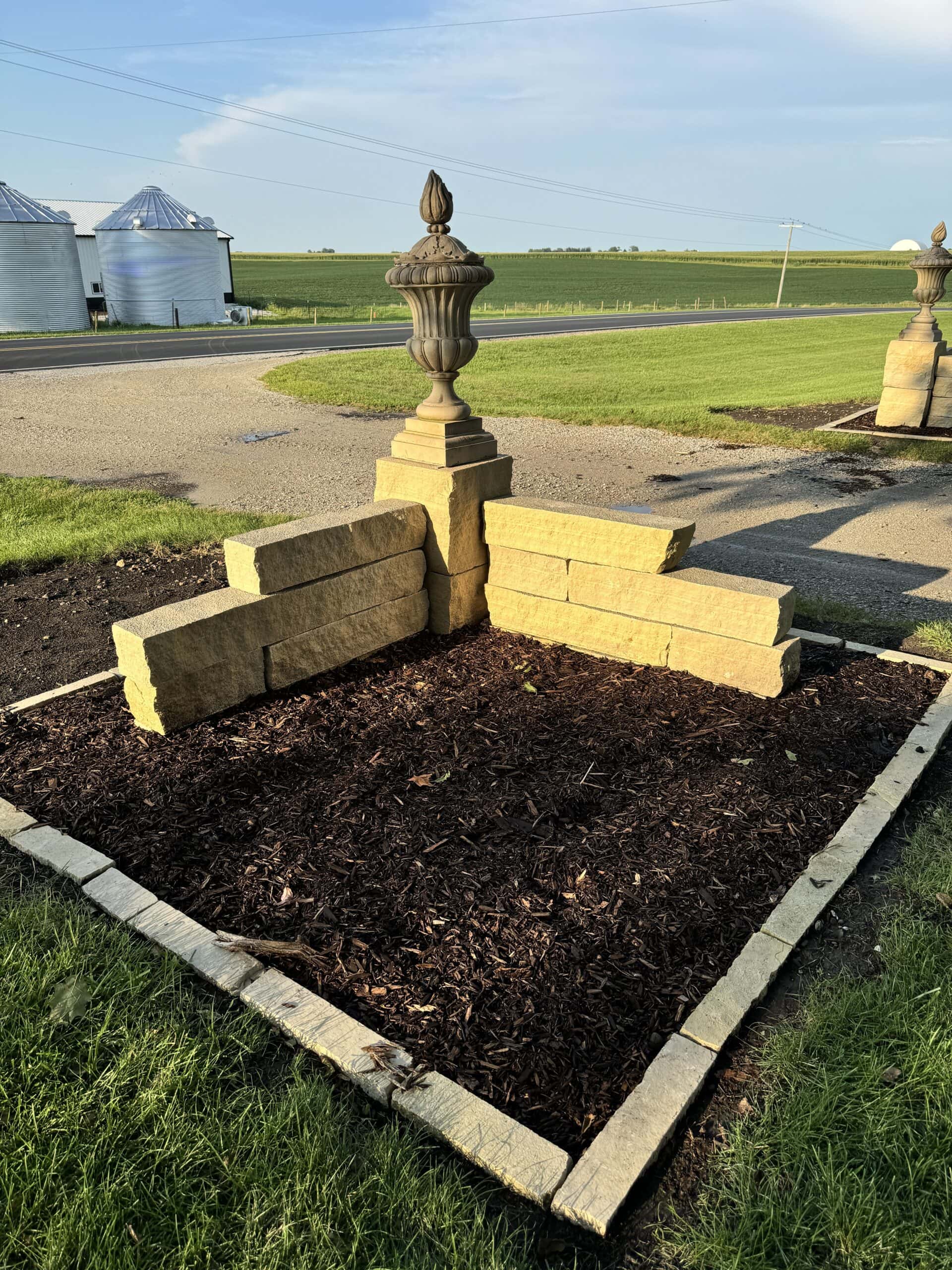 The backside of a large stone urn on top of a stone driveway entrance.