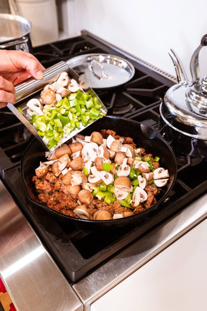 Vegetables get added to sausage browning on the stove.