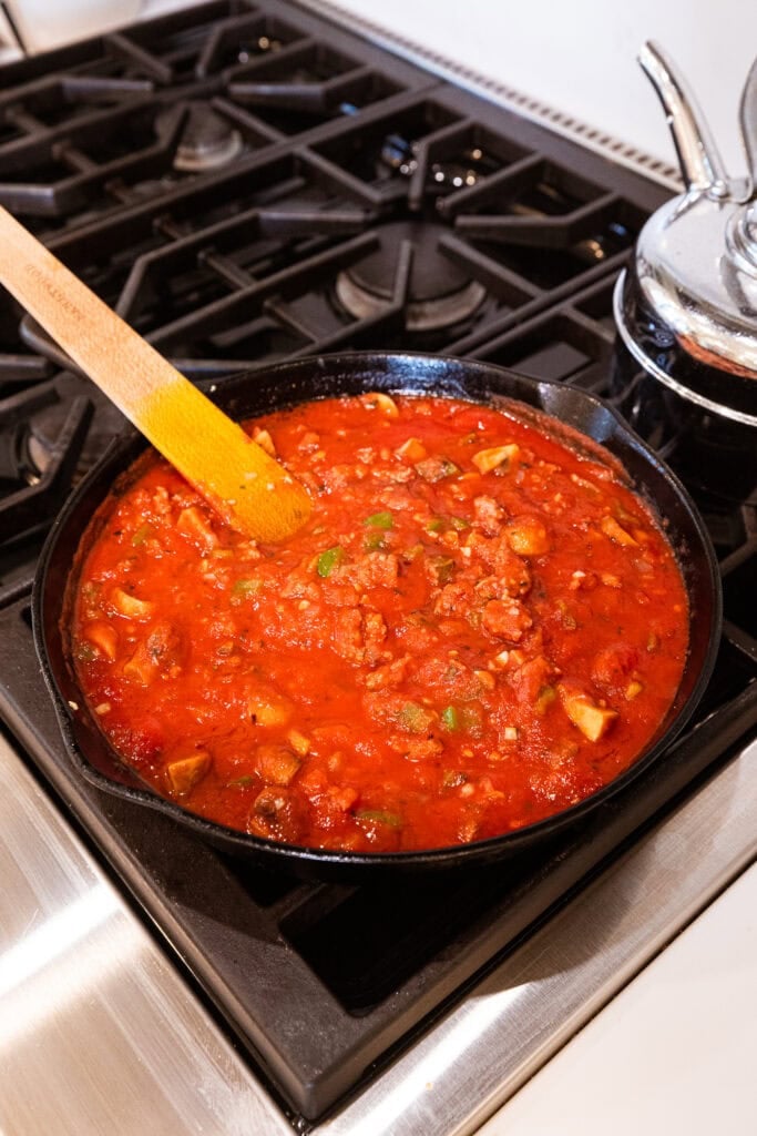 Sausage cooks in tomatoes on the stove.