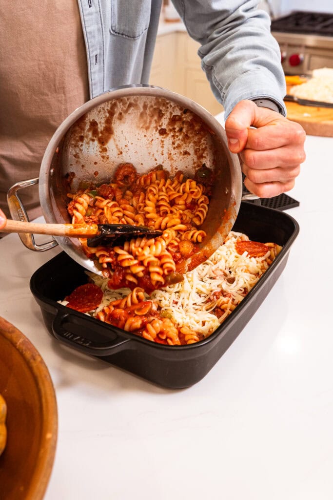 Pouring a pasta mixture into a baking dish.