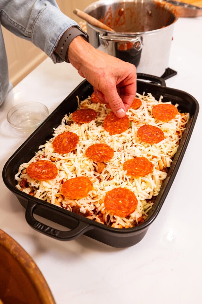 Layering pepperoni overtop mozzarella on a pasta bake.