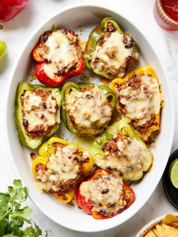 Stuffed peppers topped with shredded cheese in a baking dish.