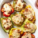 Large white serving platter with stuffed peppers with melted cheese on top.