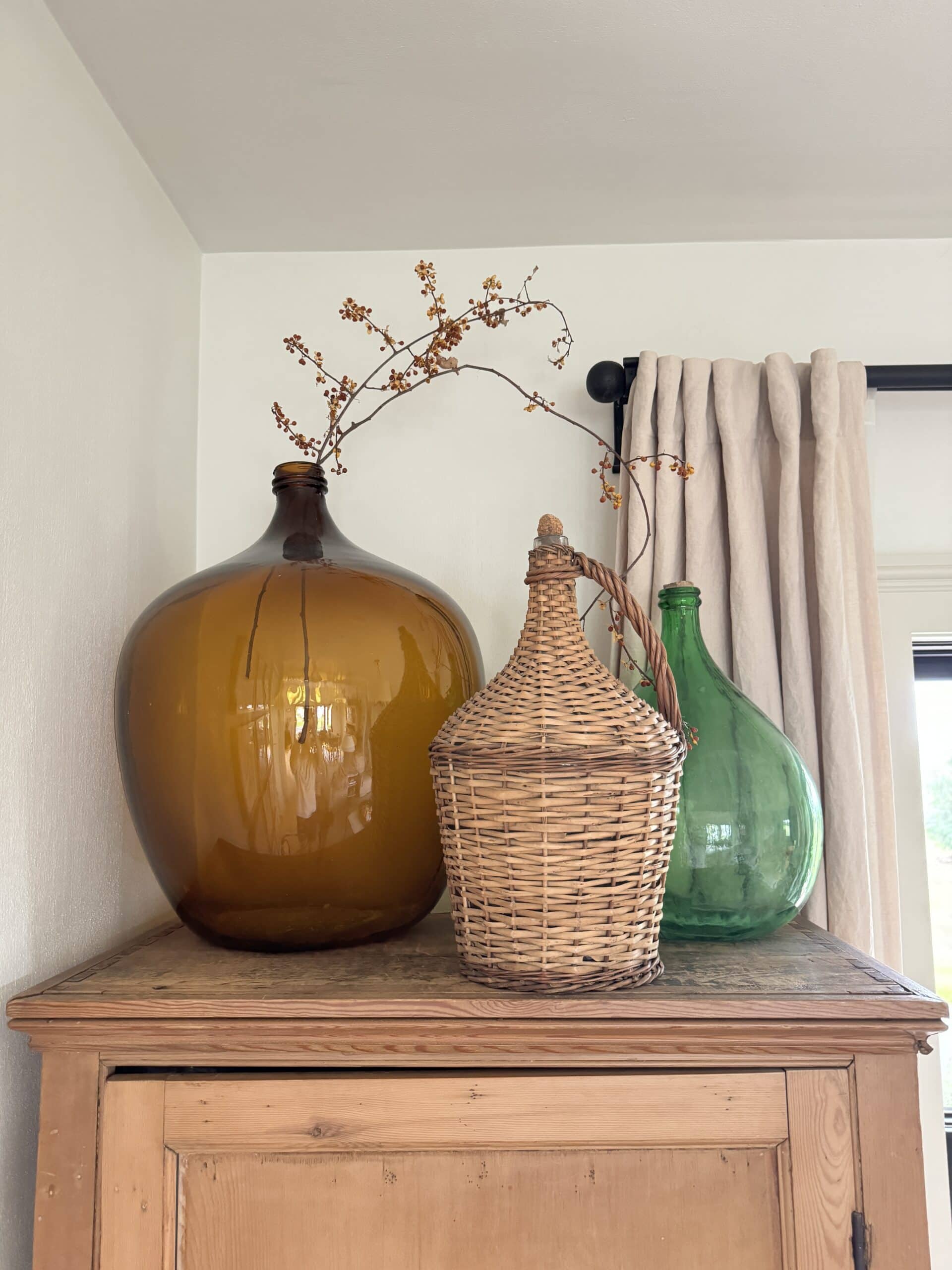 Pine cabinet in living room with large glass vessels on top one with sprig of bittersweet.