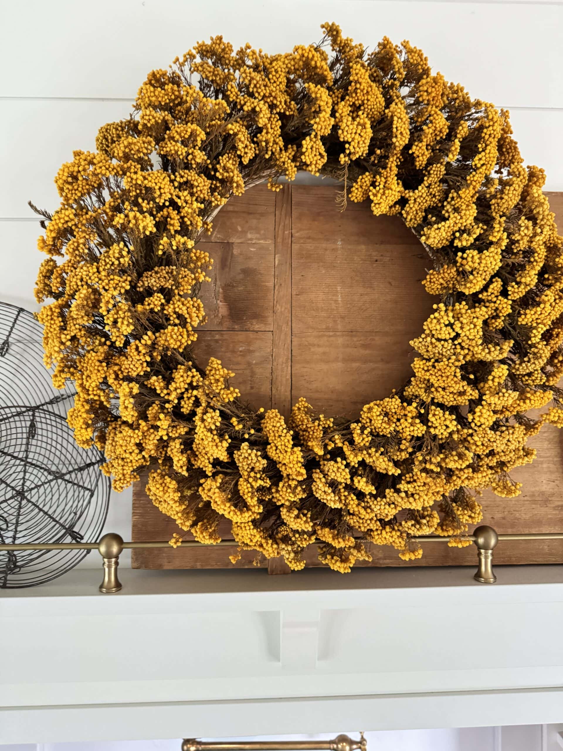 Yellow wreath hanging on a hood with cutting board and wire cooling rack behind.