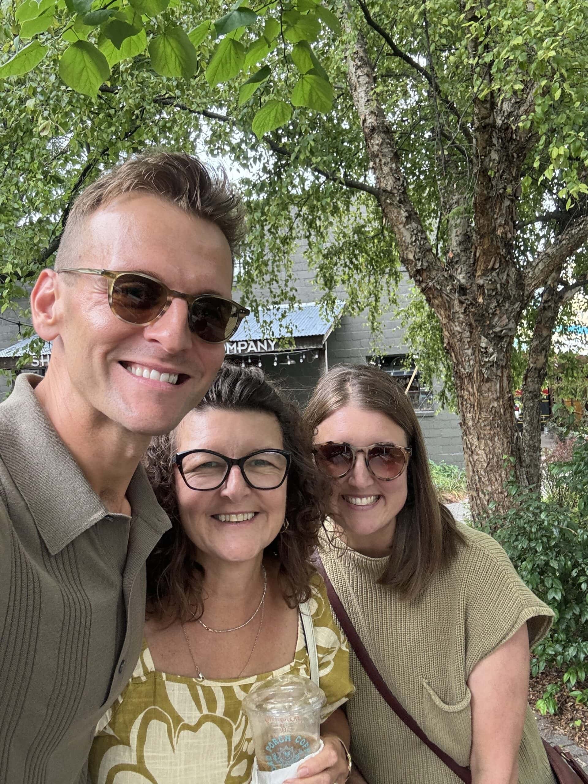 Kaleb Wyse wearing sunglasses standing in a group hug with his mom and sister while on a trip.