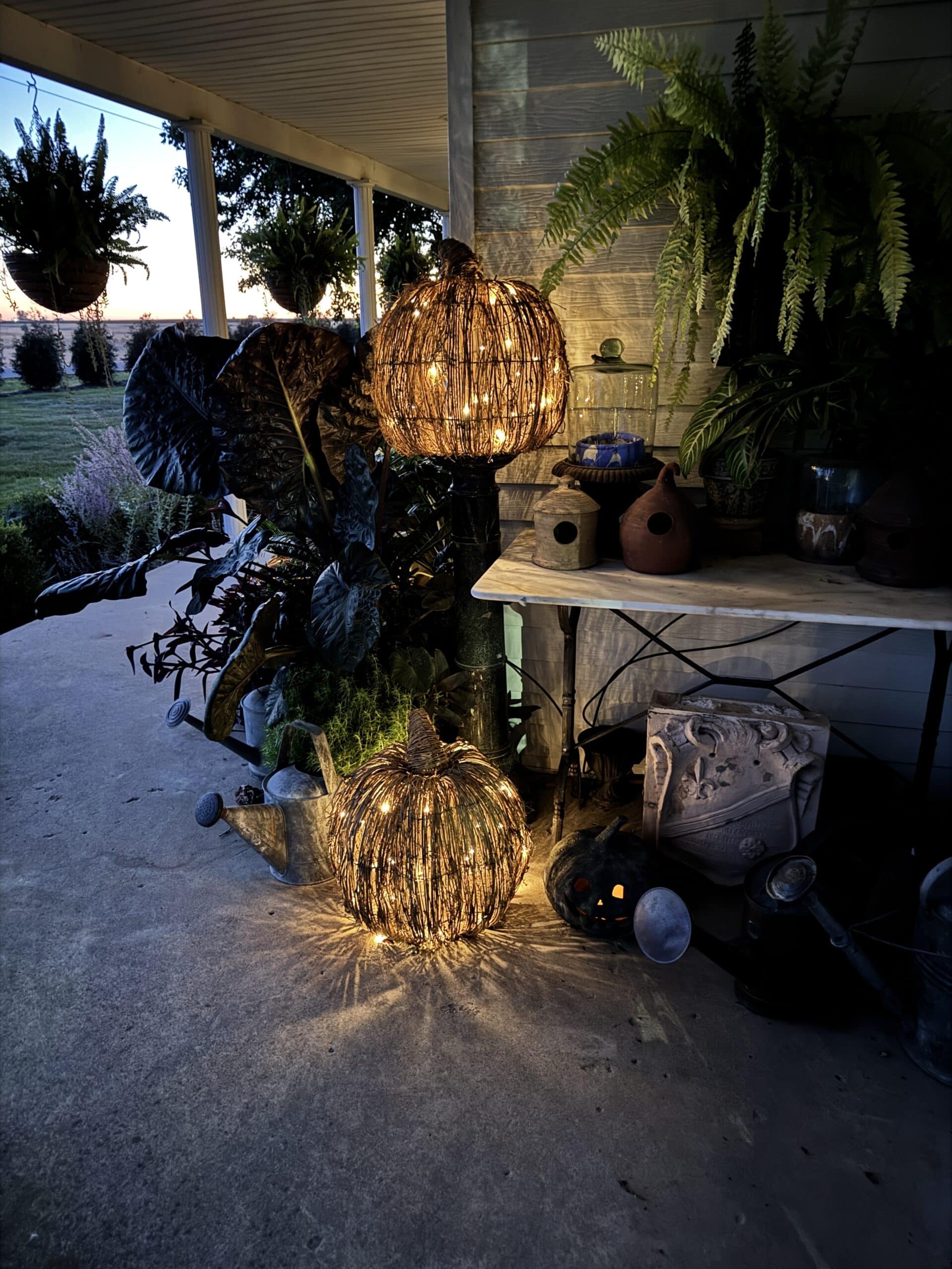 Lit up wicker pumpkins on a front porch in dusk light.