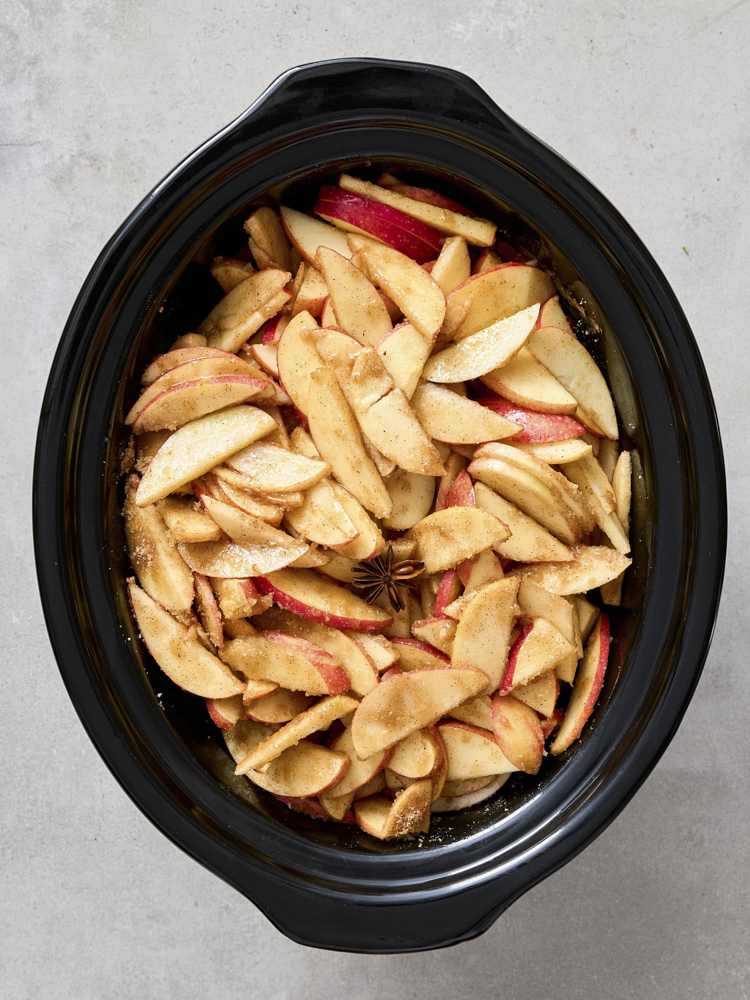 Slow cooker with sliced apples and spices for apple butter.