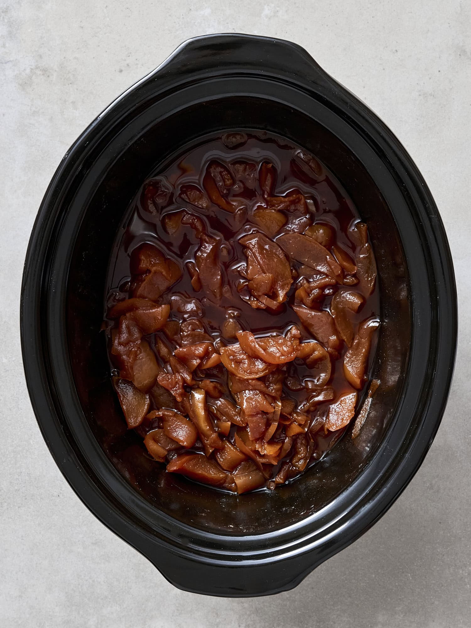 Slow cooker with dark brown apple butter mixture cooking.