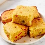 Plate filled with stacked pieces of jalapeño cornbread with green and red specks showing.