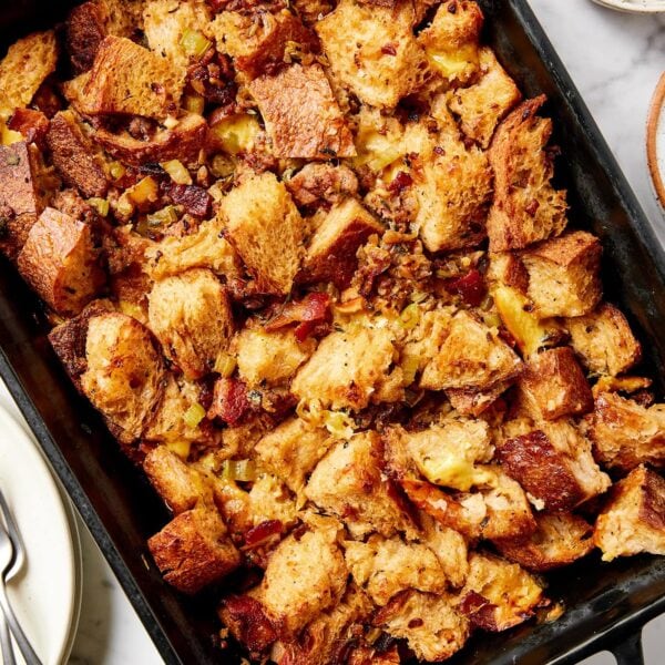 Black baking pan filled with sausage stuffing with herbs and plates to the side all on marble surface.