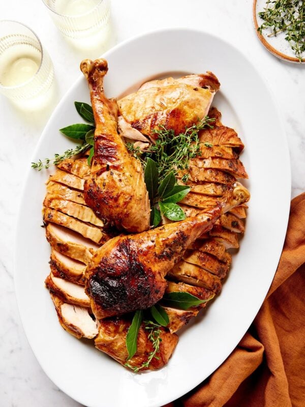White platter filled with turkey after being cooked with glasses of white wine and fresh herbs.