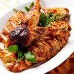 White platter filled with pieces of cowboy butter turkey with skin on it along with more herbs.