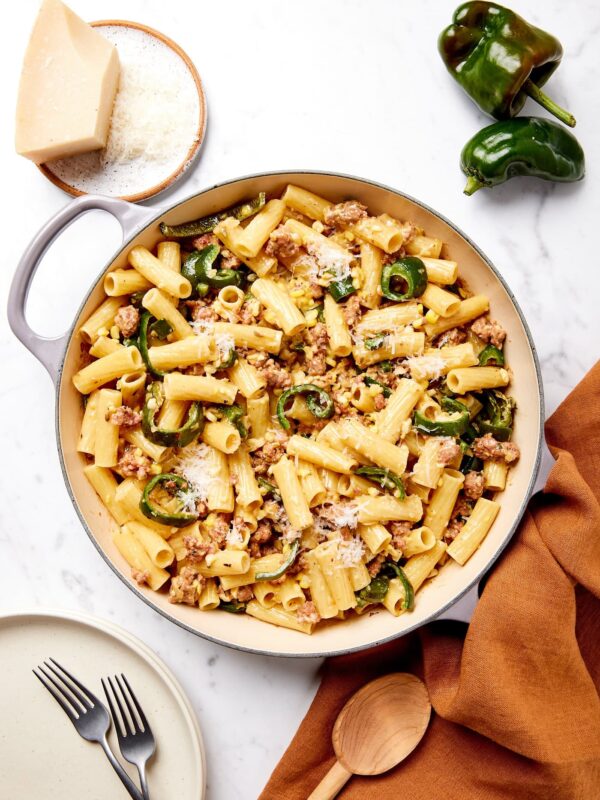 White marble surface with large pot filled with creamy sausage pasta with sweet corn and poblano peppers.