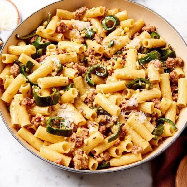 Marble surface with bowl filled with creamy sausage pasta with brown towel to the side.