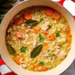 Red Dutch oven filled with leftover turkey soup with carrots, turkey, and bay leaves on top.