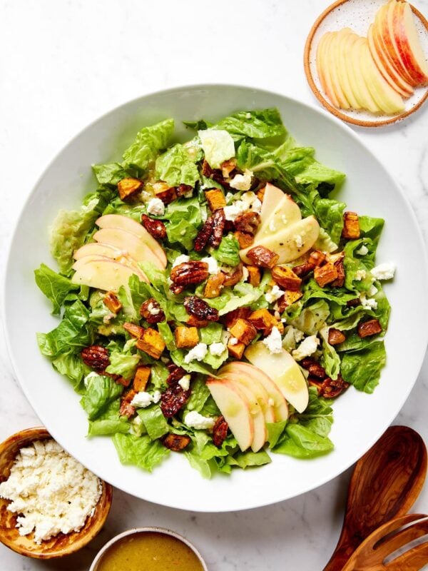 White marble surface with large white bowl filled with sweet potato salad with apples and feta to the side.