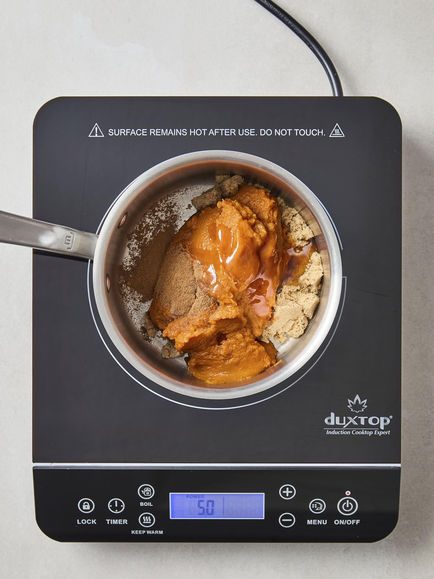 Saucepan on stove with sugar, honey, spices, and pumpkin puree.