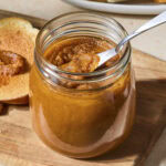 Jar filled with pumpkin butter with piece of toast in background.