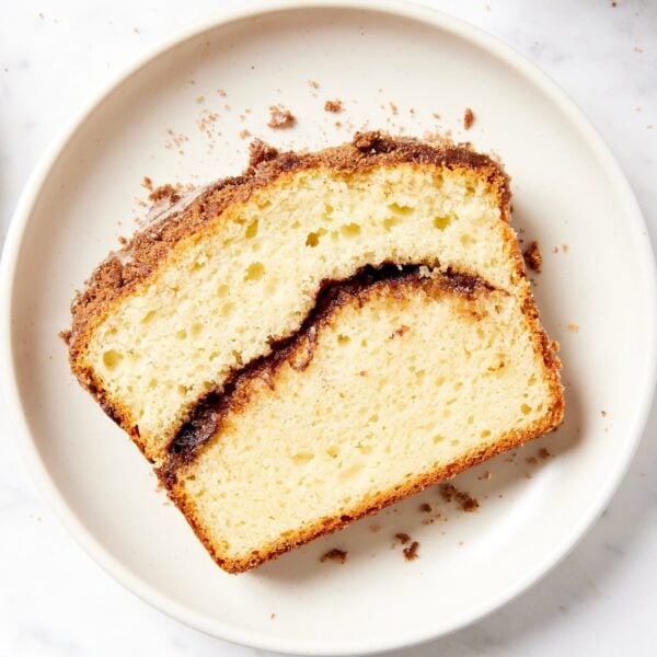White plate on marble surface with slice of coffee cake with cinnamon in the center.