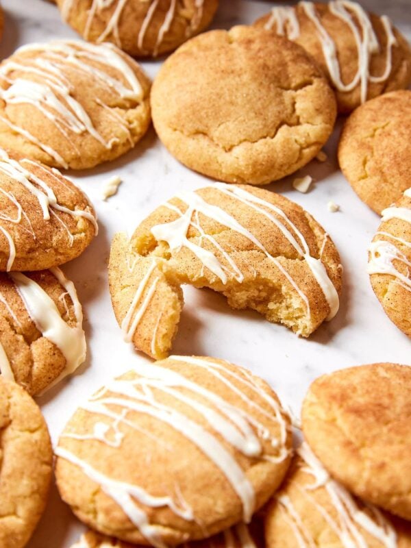 Pile of brown butter Snickerdoodle cookies on white marble with drizzle of white chocolate over the top.