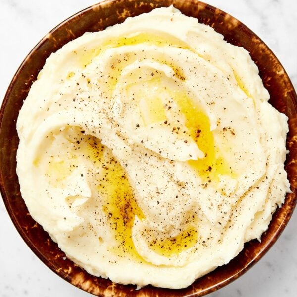 Brown bowl filled with creamy mashed potatoes with sprinkling of black pepper and butter on top.