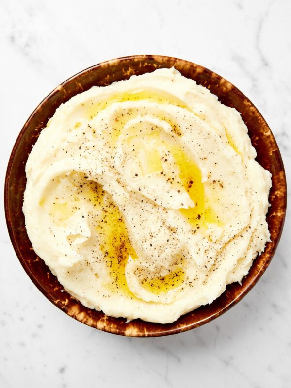 Brown bowl filled with creamy butter-covered mashed potatoes sitting on a marble surface.