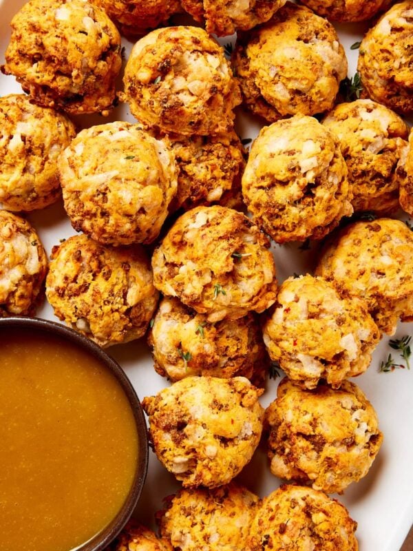 Small puffs made from sausage and sweet potato sitting on a white platter with a honey mustard sauce to the side.