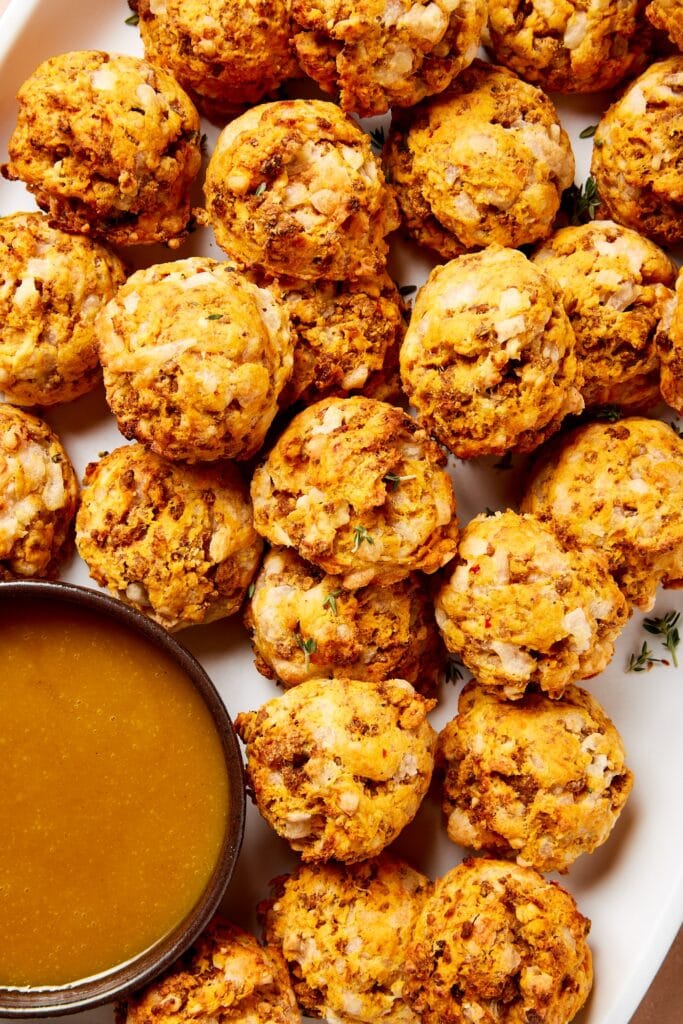 Small puffs made from sausage and sweet potato sitting on a white platter with a honey mustard sauce to the side.