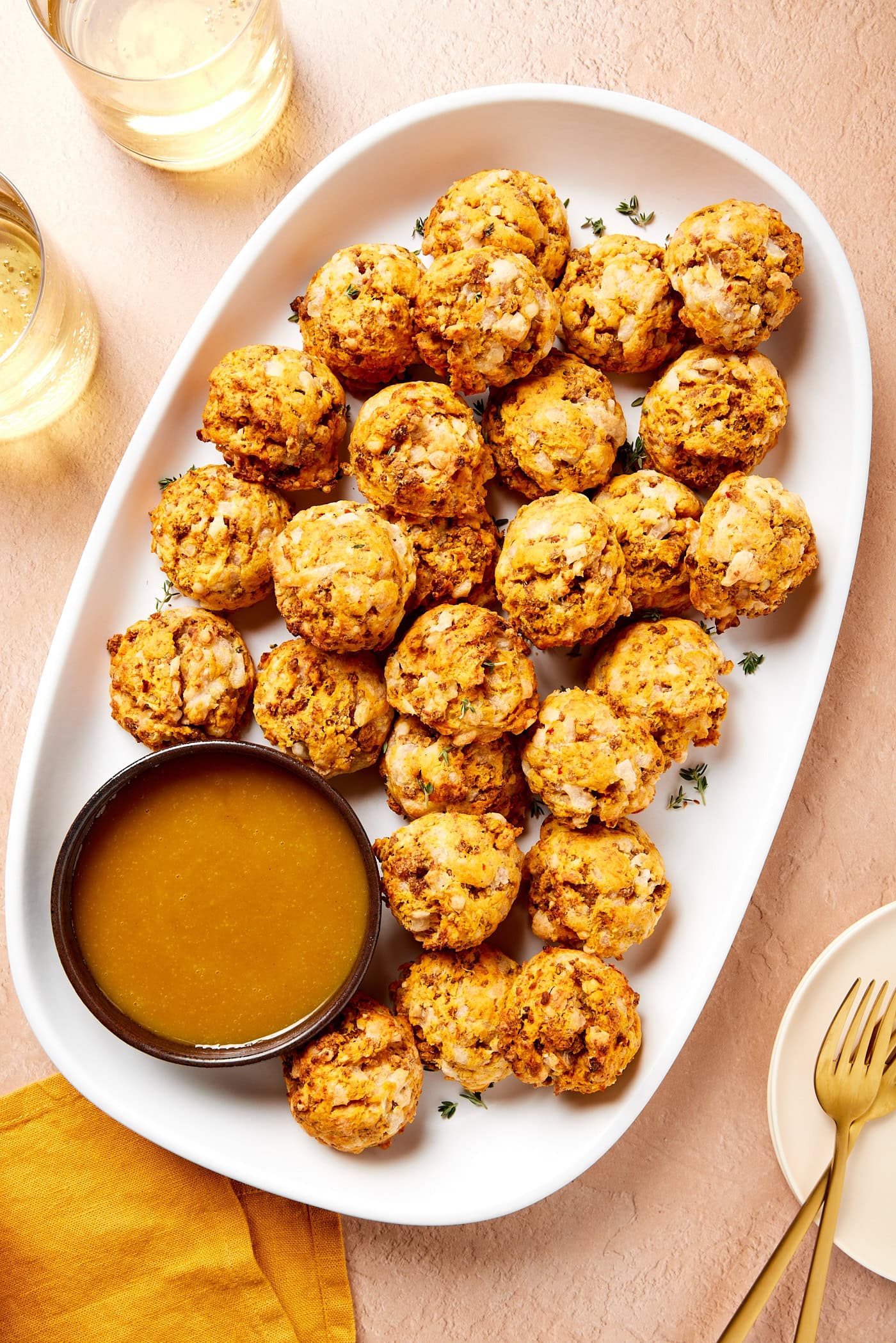Sausage and sweet potato puffs rest on a serving platter with a dressing.