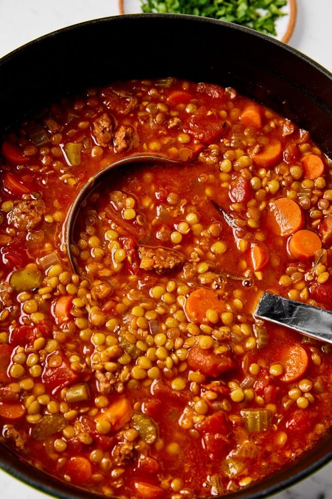 Sausage and lentil soup in a pot with a ladle.