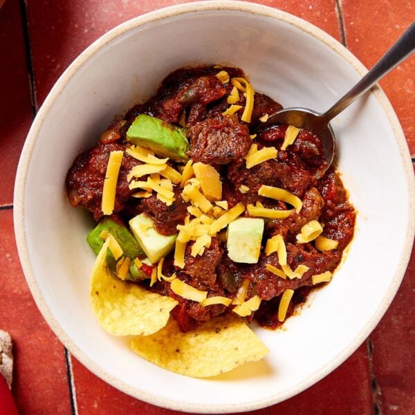 A bowl of chili with tortilla chips and cheese and avocado.