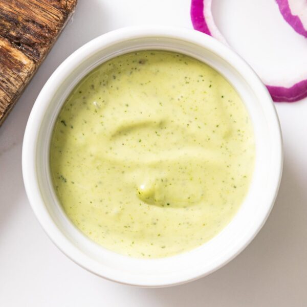 White bowl filled with dill aioli with a green color on white surface.