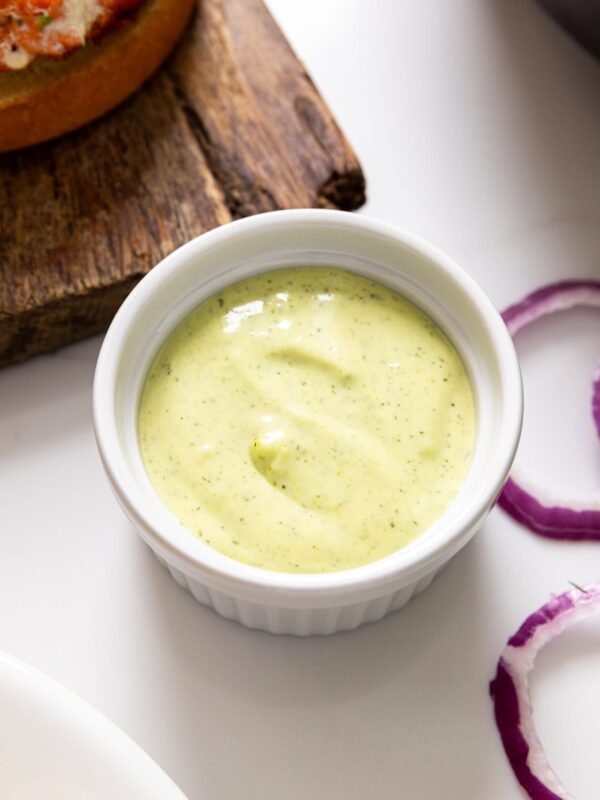 White dish filled with green-colored dill aioli sauce on white countertop.