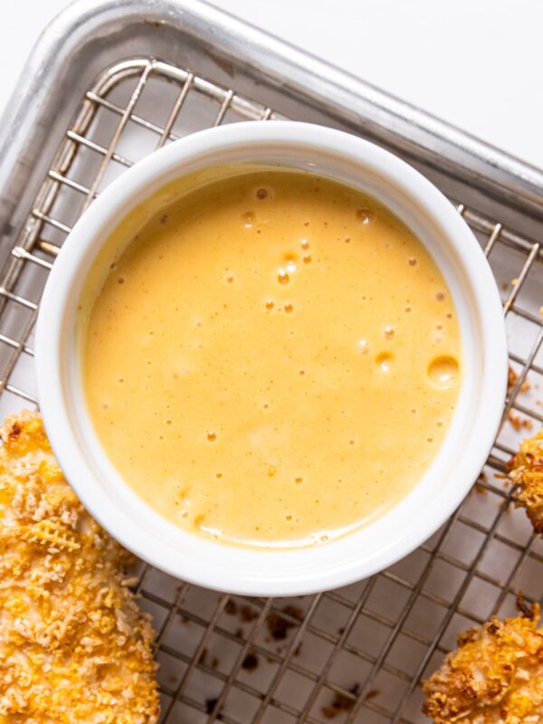 White bowl with light orange colored honey mustard sauce with chicken strips to the side.