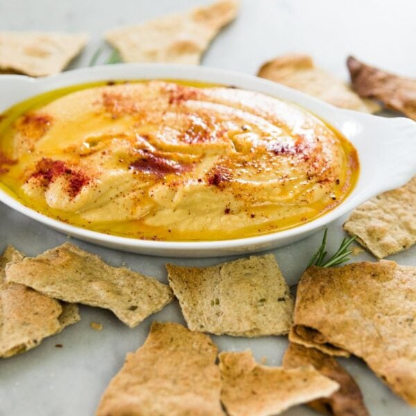Rosemary homemade crackers broken into pieces with a bowl of hummus in the background.