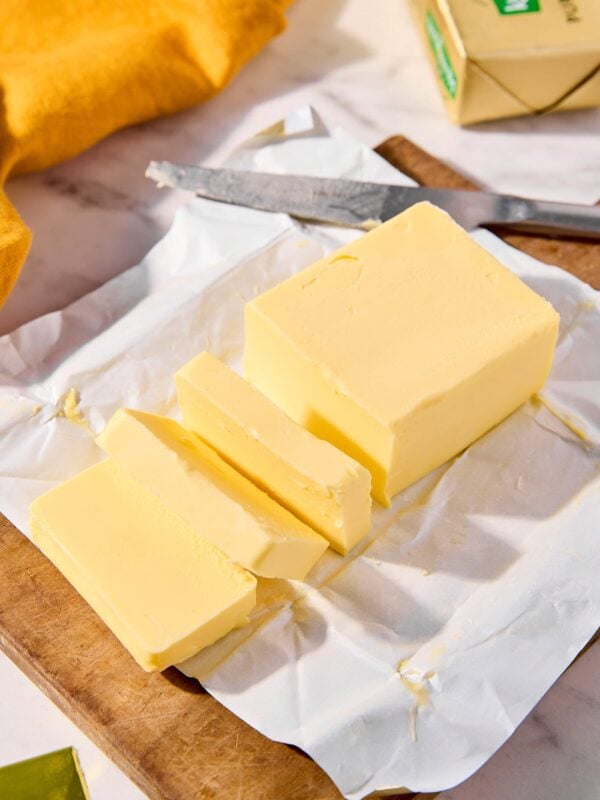 Large stick of butter sliced into pieces sitting on it's wrapping paper.