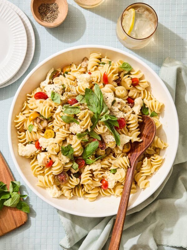 White bowl filled with Caprese pasta salad with spoon scooping out a portion.